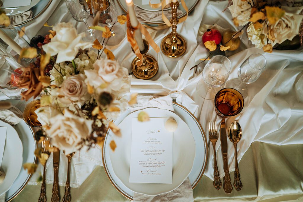 Close-up of wedding place setting with menu, gold cutlery and neutral floral centrepiece by Wonderland Blooms, East Yorkshire wedding florist.