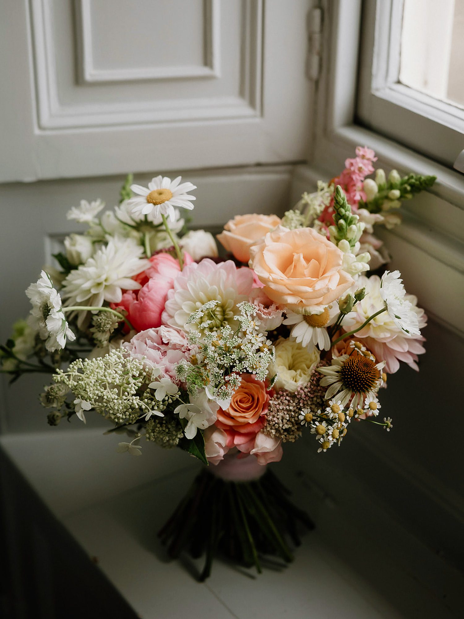 Garden-style bridal bouquet with peach roses, daisies, pink peonies, and soft seasonal florals.